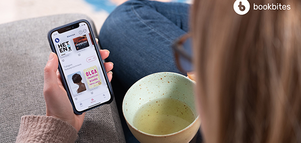 Foto tatt over skuldra til person som sit og drikk te og les e-bok på mobilen