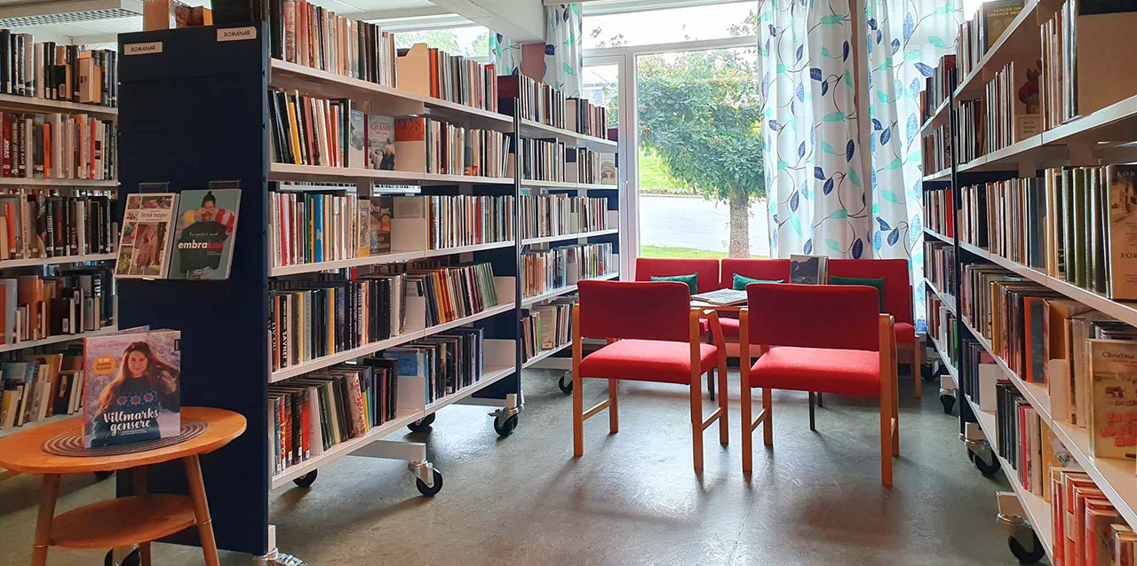Foto av bokhyller i eit bibliotek, med ei raud sitjegruppe mellom
